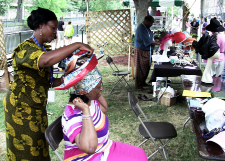 Faith Izevbijie ties a headwrap while Samuel Brown sews hats.
